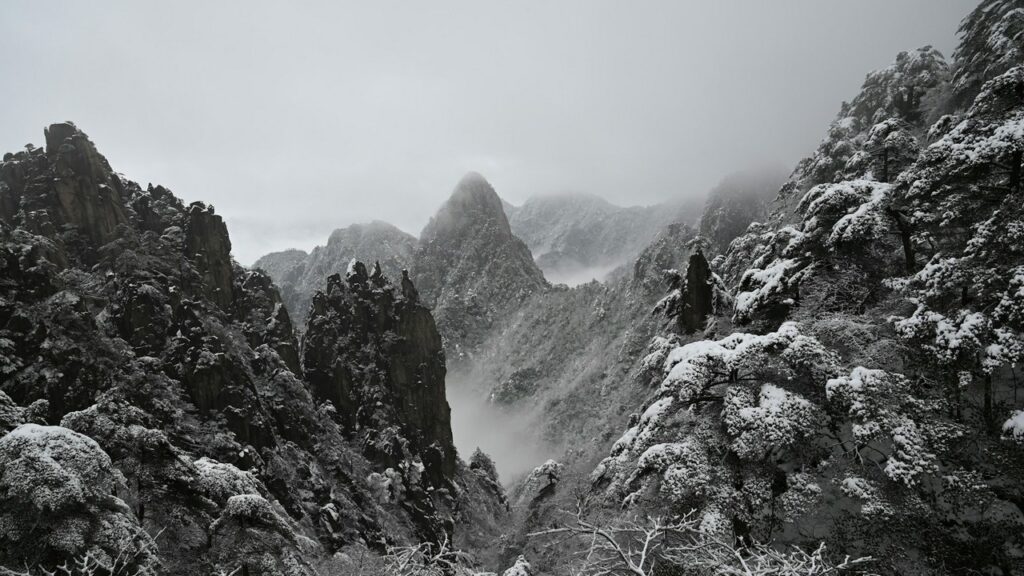 a snowy mountain range with trees and clouds yellow mountain china
